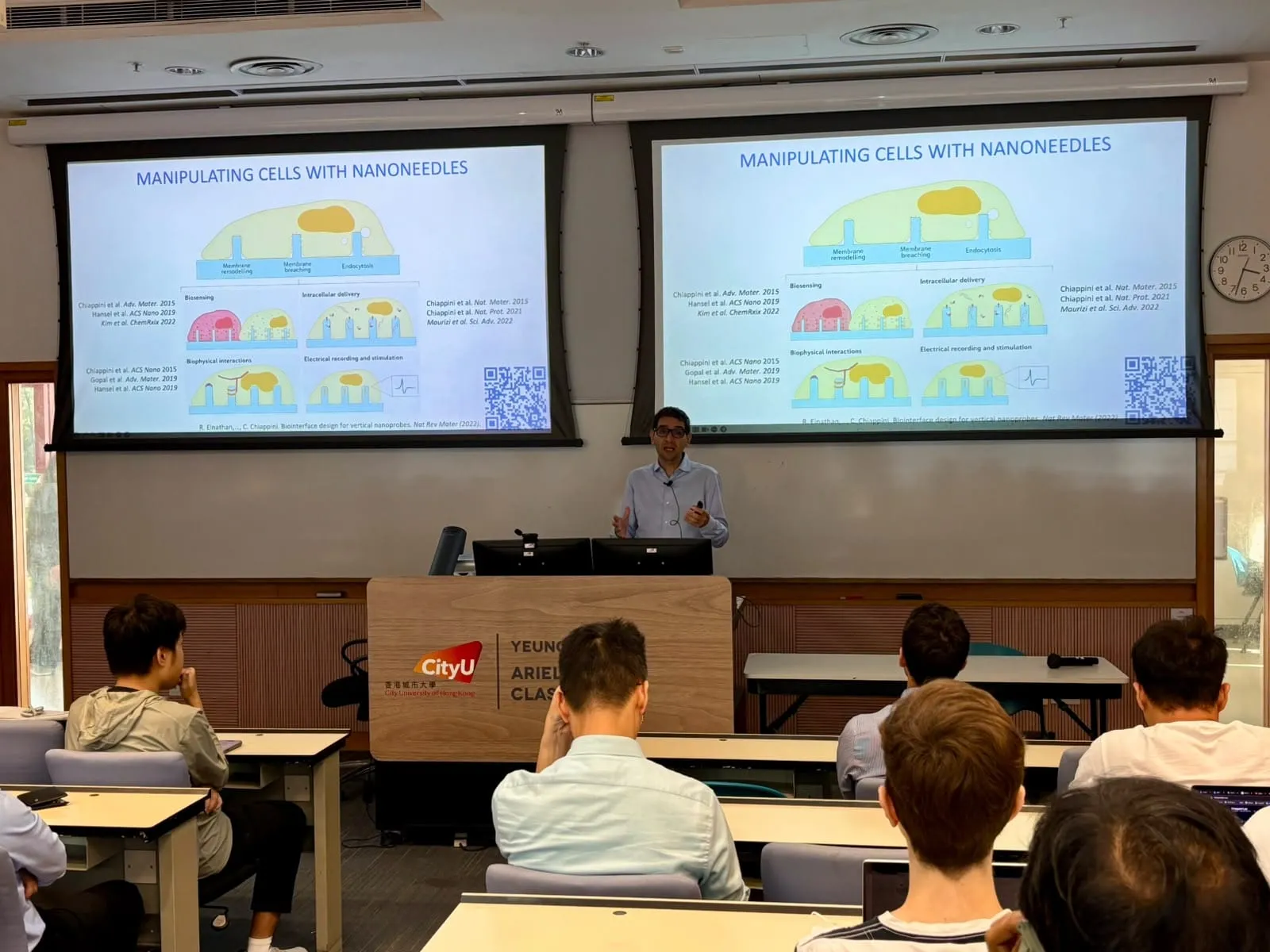 Ciro Chiappini speaking at the CityU College of Biomedicine seminar, with a slide titled ‘Manipulating cells with nanoneedles’ on two screens and the audience in the foreground
