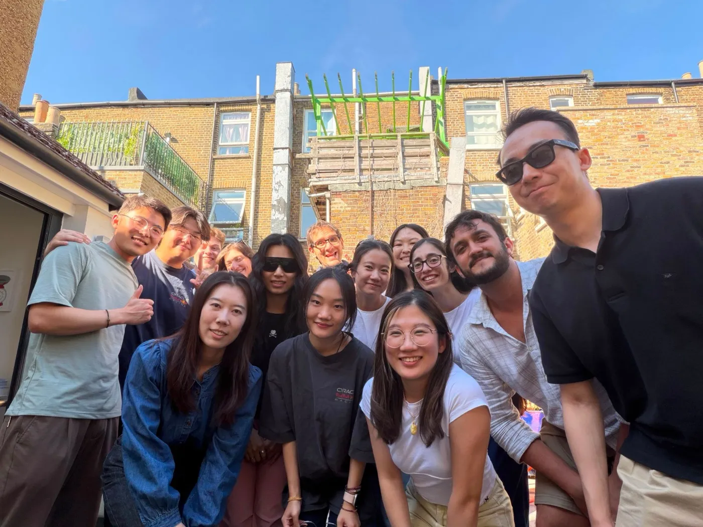 Around fifteen lab members squeezed into a smiling group selfie on a sunny rooftop terrace.